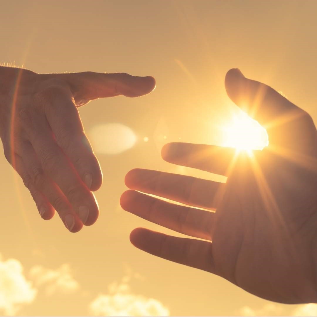 Une main tendue vers une autre avec de la lumière entre elles, symbolisant le soutien, l’accompagnement et la transformation personnelle.